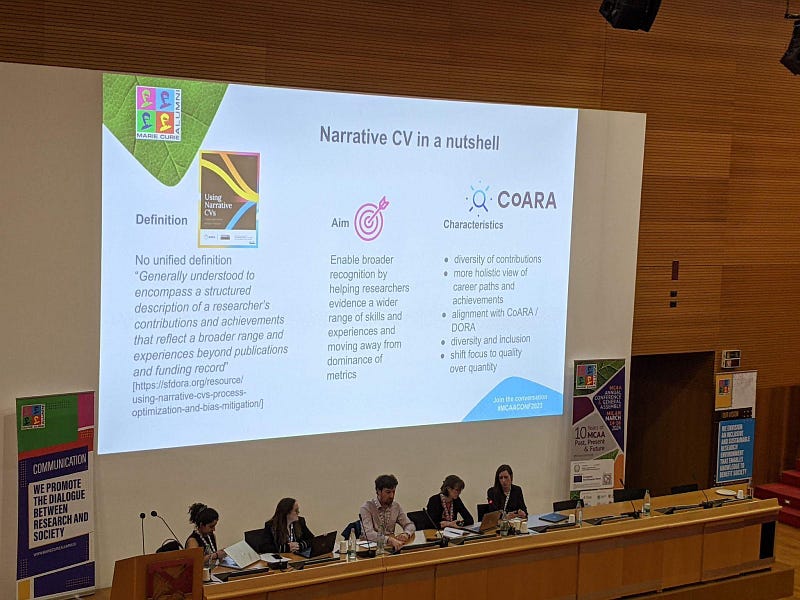 The panel of speakers, in the background a slide about definition, aim and characteristics of a narrative CV. Photo taken by the author
