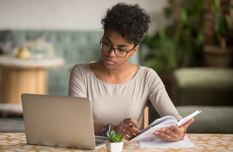 Focused student looking at laptop holding book